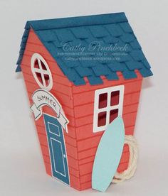 a small red house with a surfboard on the door and windows, sitting in front of a white background