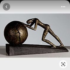 a bronze statue is sitting on top of a wooden block with a ball in the shape of a human figure