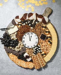 a clock made out of food on top of a plate with crackers and nuts