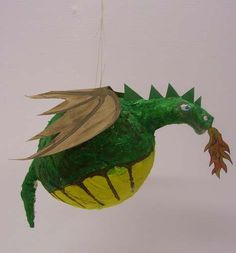 a green and yellow dragon ornament hanging from a string on a white wall