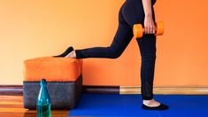 a woman is doing exercises with dumbbells on a mat in front of an orange wall