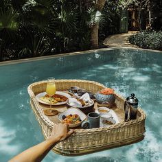 a person holding a wicker basket with food on it in front of a swimming pool