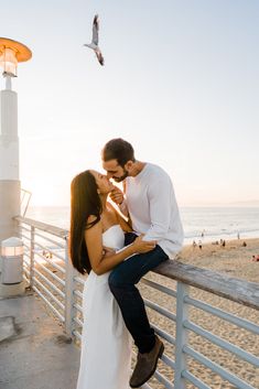 a man and woman kissing on the beach next to a light pole with seagulls flying in the background