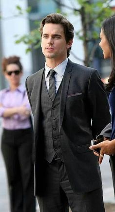 a man in a suit and tie standing on the street with other people behind him