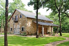 an old stone house in the middle of a grassy area with trees and grass around it