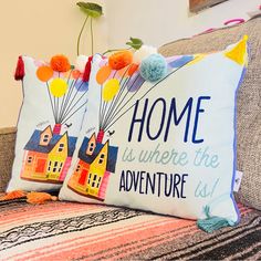 two decorative pillows sitting on top of a couch in front of a pillow that says home is where the adventure is