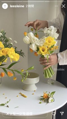 two people are arranging flowers in vases on a table with white and yellow flowers