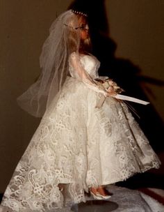 a barbie doll dressed in a wedding dress and veil holding a knife with her hand