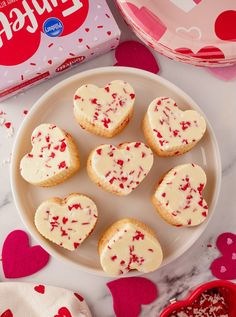 valentine's day cookies on a plate next to a box of candy