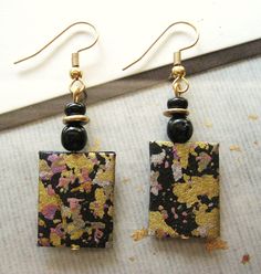 two square shaped earrings with black beads and gold leaf print on the front, hanging from earwires