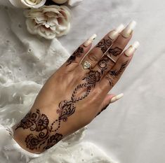 a woman's hand with henna tattoos on it and flowers in the background