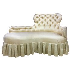 a white chaise lounge with pleated skirting on the bottom, and buttoned back