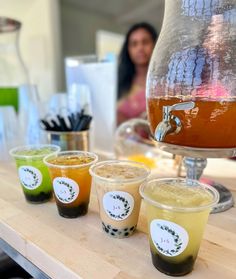 there are many cups on the table with different drinks in them and one has a beverage dispenser