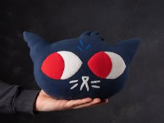 a hand holding a blue cat pillow with red eyes