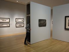 a man is walking through an art gallery with paintings on the wall and in the background