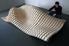 a man sitting on the floor next to a large wooden structure that is shaped like a wave