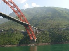 a large red bridge spanning over a body of water with mountains in the back ground