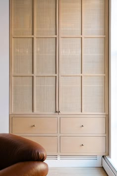 a brown leather chair sitting in front of a wooden cabinet with glass panels on it