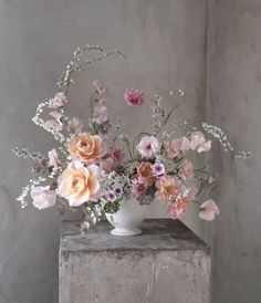 a white vase filled with lots of pink and orange flowers on top of a table