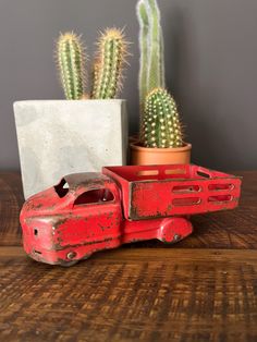 an old red toy truck next to a cactus