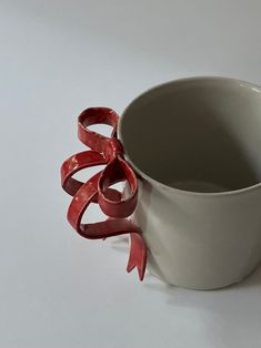 a white cup with red ribbon wrapped around it's side on a white surface