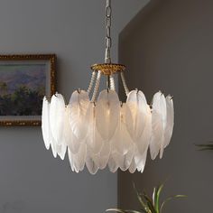 a white chandelier hanging from a ceiling in a room with paintings on the wall