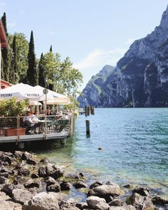 an outdoor restaurant on the water with mountains in the background