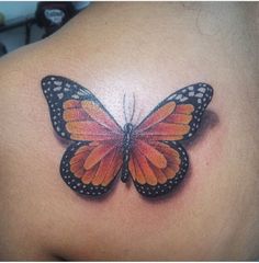 an orange and black butterfly tattoo on the back of a woman's shoulder