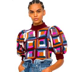 a woman with braids wearing a colorful sweater and overalls, standing in front of a white background