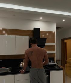 a man with no shirt standing in front of a kitchen counter and stove top oven