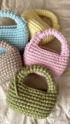 four crocheted purses sitting on top of a white bed next to each other