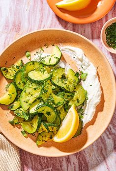 a bowl filled with cucumbers, sour cream and lemon wedges on top of a table