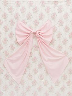 a pink bow is hanging on the wall in front of floral wallpaper with white and pink flowers