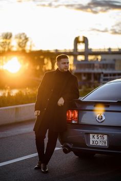 a man standing next to a car in the street at sunset or sunrise with his hands on his hips