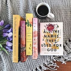 some books are laying on a blanket next to a cup of coffee and purple flowers