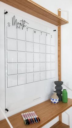 a dry erase board on a wooden shelf with markers and pencils in front of it