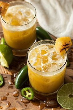 two glasses filled with drinks sitting on top of a wooden table next to green peppers