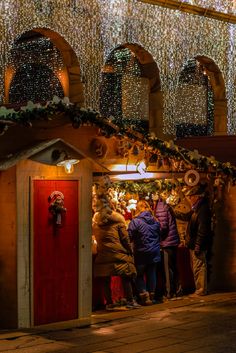 people are standing in front of a small christmas shop with lights on the roof and decorations all around it