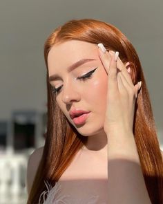 a woman with long red hair holding her hand up to her face