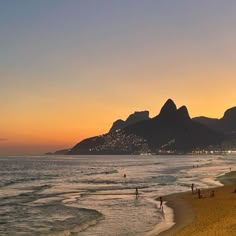 people are walking on the beach at sunset with mountains in the backgrouund