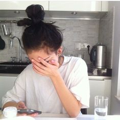 a woman sitting at a kitchen table with her hands on her face and looking down