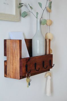 a wooden shelf with hooks and keys hanging on the wall next to a vase filled with flowers