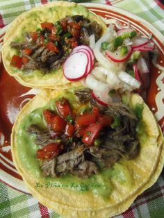 two tortillas with meat, onions and tomatoes on a red plate sitting on a checkered table cloth