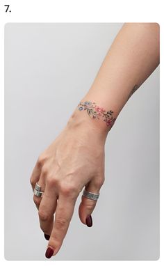 a woman's hand with two rings on it and a flower tattoo on the wrist