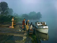 three people standing on a dock next to a small boat in the foggy water