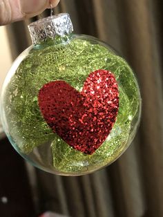 a hand holding a glass ornament with a red and green heart on it