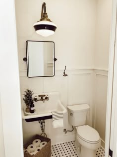 a white toilet sitting next to a sink in a bathroom under a mirror and light