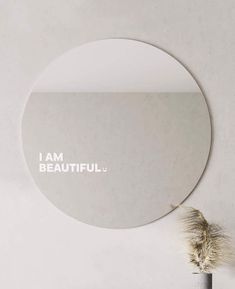 a round mirror with the words be kind on it next to a potted plant