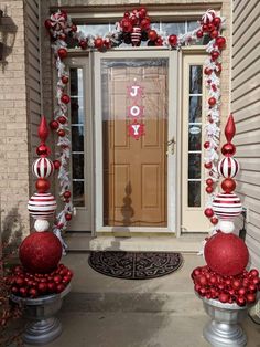 two red and white christmas decorations on top of urns in front of a door