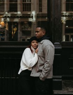 a man and woman standing next to each other in front of a tall building on a city street